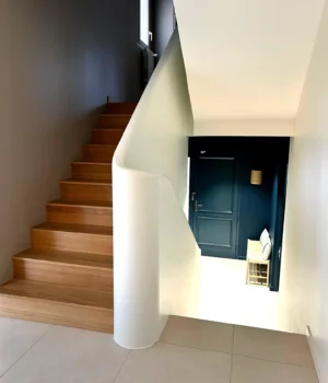 Cage d’escalier rénovée avec peinture murale soignée et marches en bois clair.